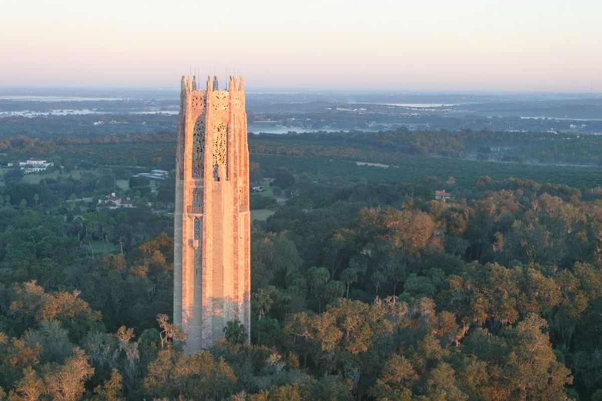 The stone Singing Tower rises above a lush green forest in Lake Wales, Florida, during a golden sunset.