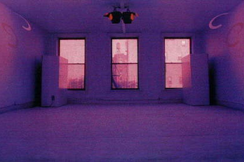 A minimalist room bathed in deep purple light with three windows showing a pink-tinted view of New York City buildings.