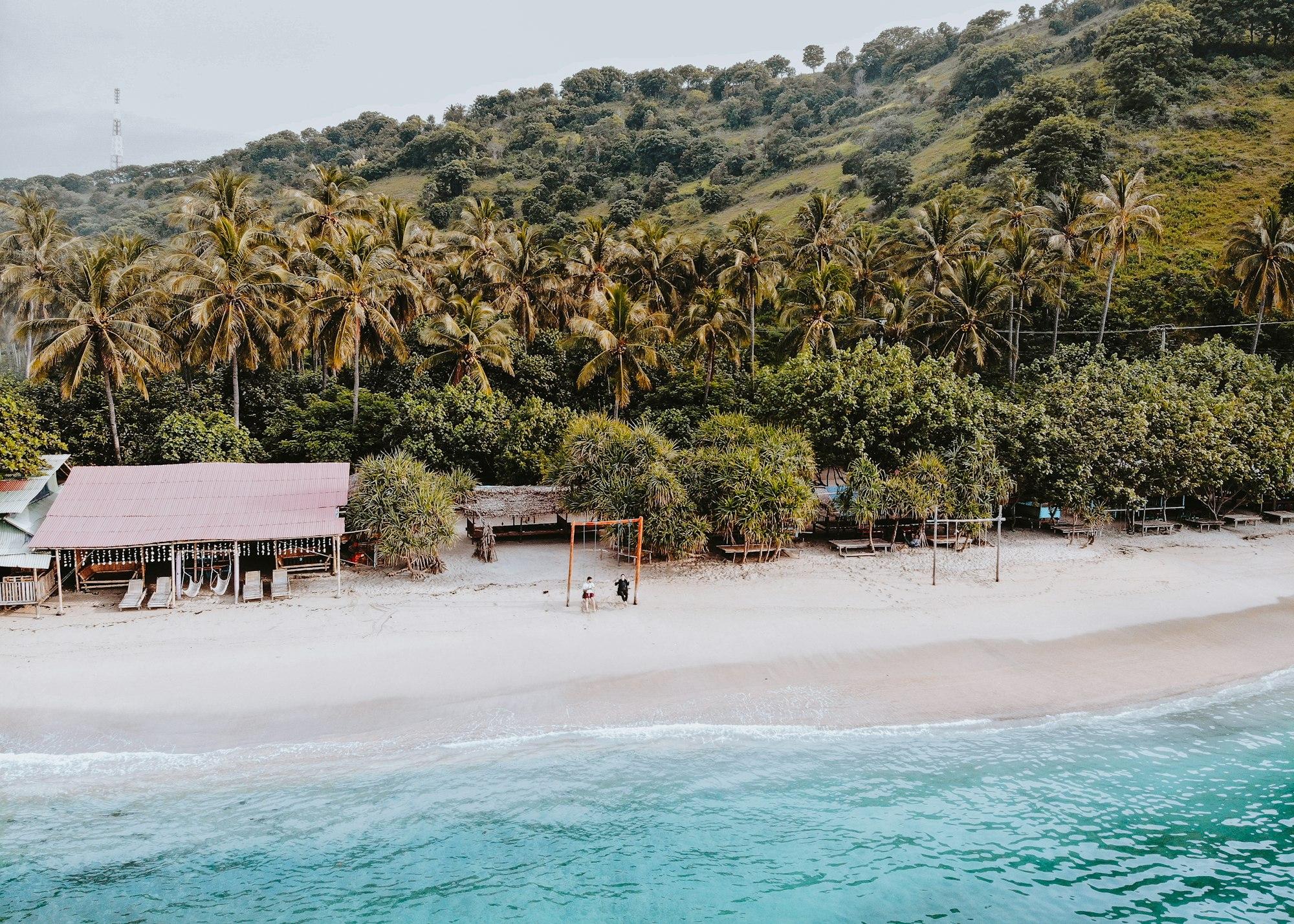 Pantai pasir putih dengan pohon kelapa dan bukit hijau di Lombok