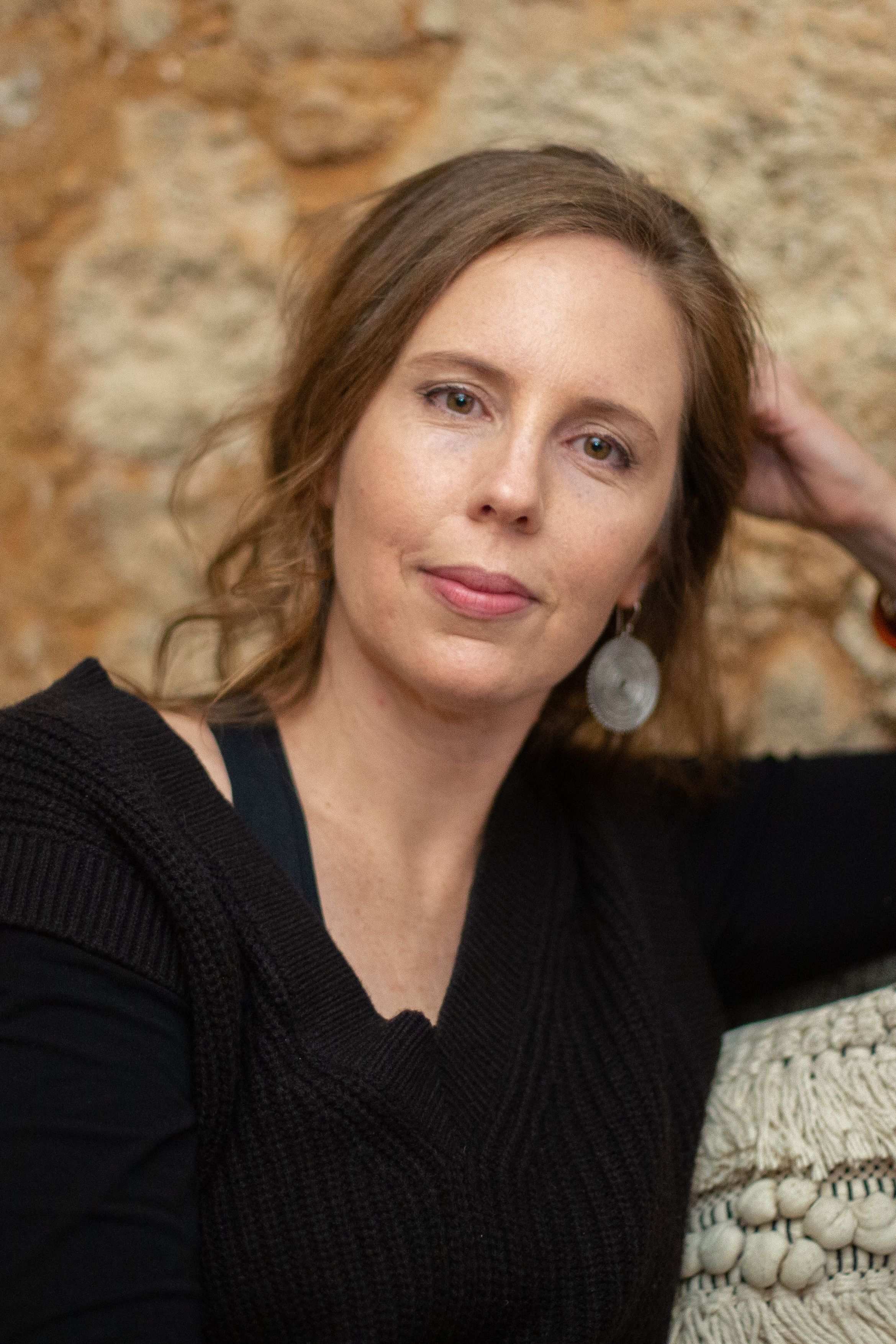 Joanna's headshot. Dressed in black, Joanna rests her elbow on the back of a chair and her head in her hand.