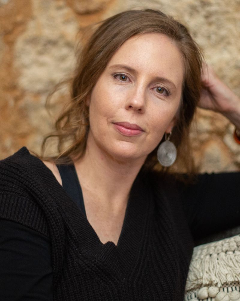 Joanna's headshot. Dressed in black, Joanna rests her elbow on the back of a chair and her head in her hand.