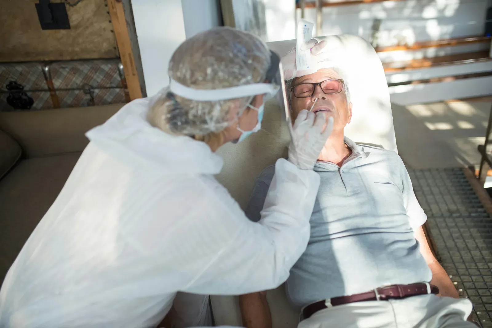Healthcare professional in protective clothing conducting a COVID-19 test on a senior adult man outdoors.
