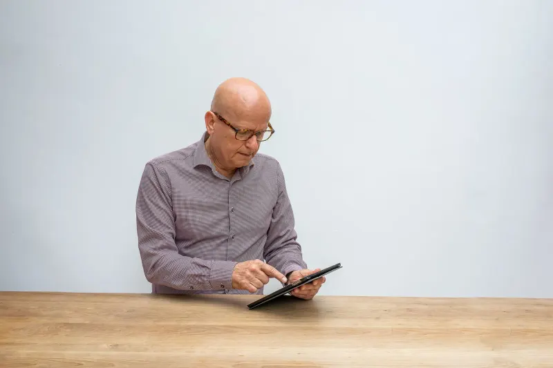 Older adult using a tablet with glasses in a well-lit room
