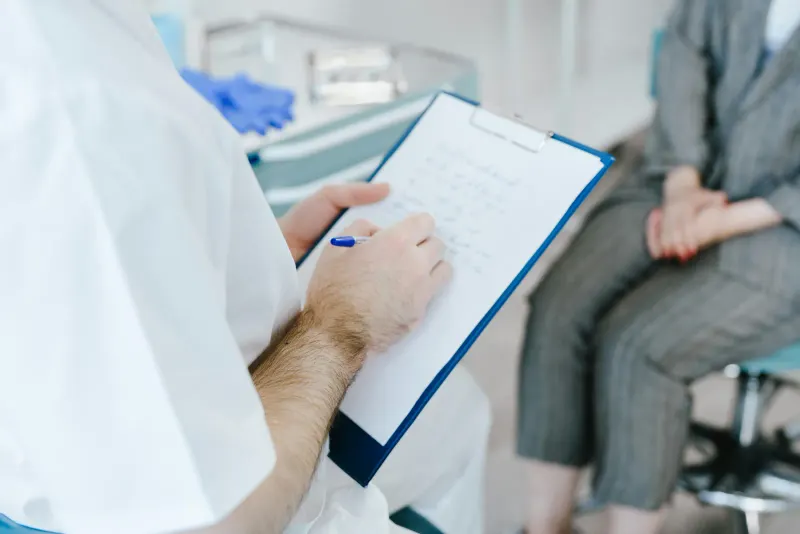 Medical professional writing patient notes on clipboard during consultation.