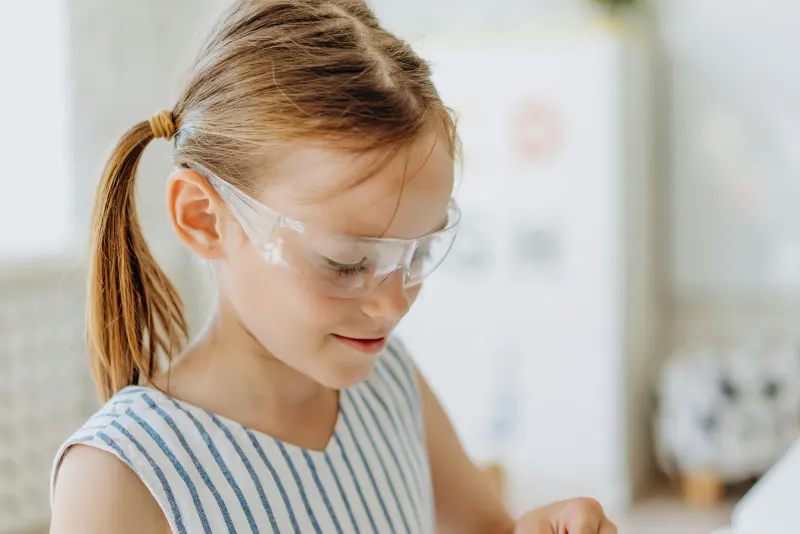 Close-up of a young girl in protective goggles indoors. Child in a striped shirt with pigtails.
