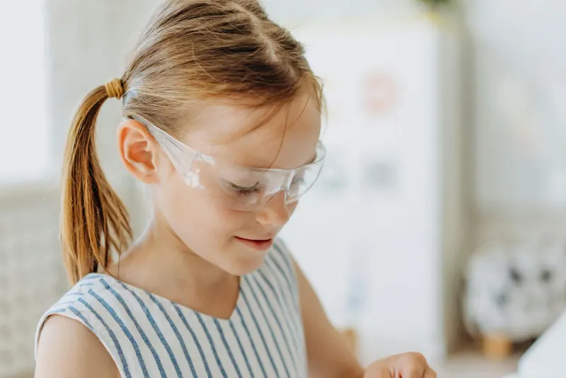Close-up of a young girl in protective goggles indoors. Child in a striped shirt with pigtails.