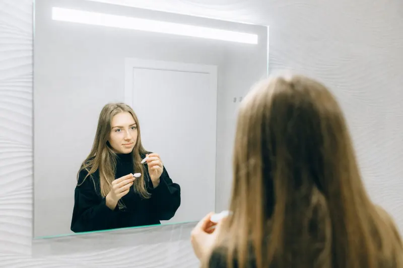 Person preparing to insert a contact lens in front of a mirror
