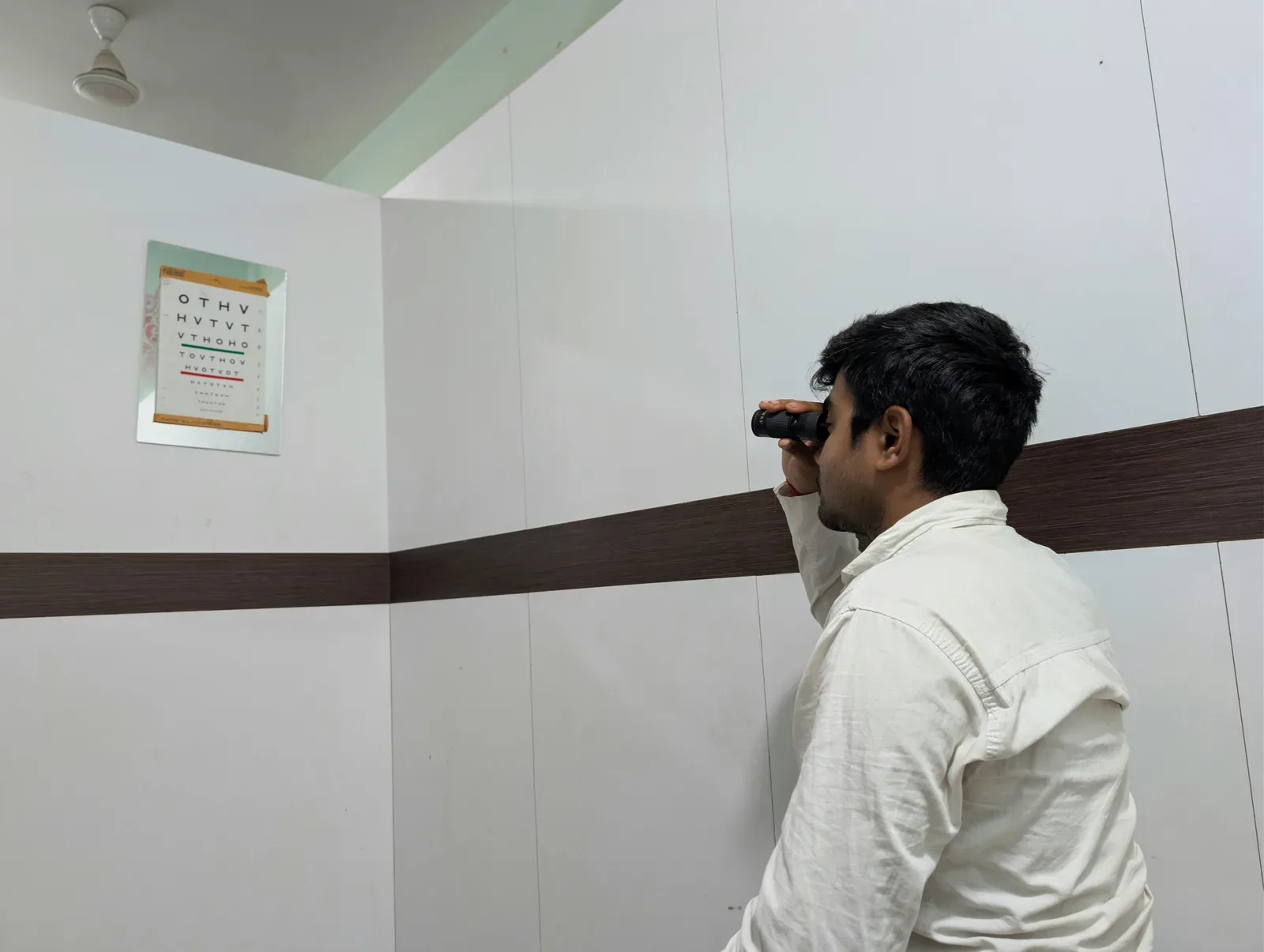 Man using binoculars to view an eye chart indoors. Vision test concept.