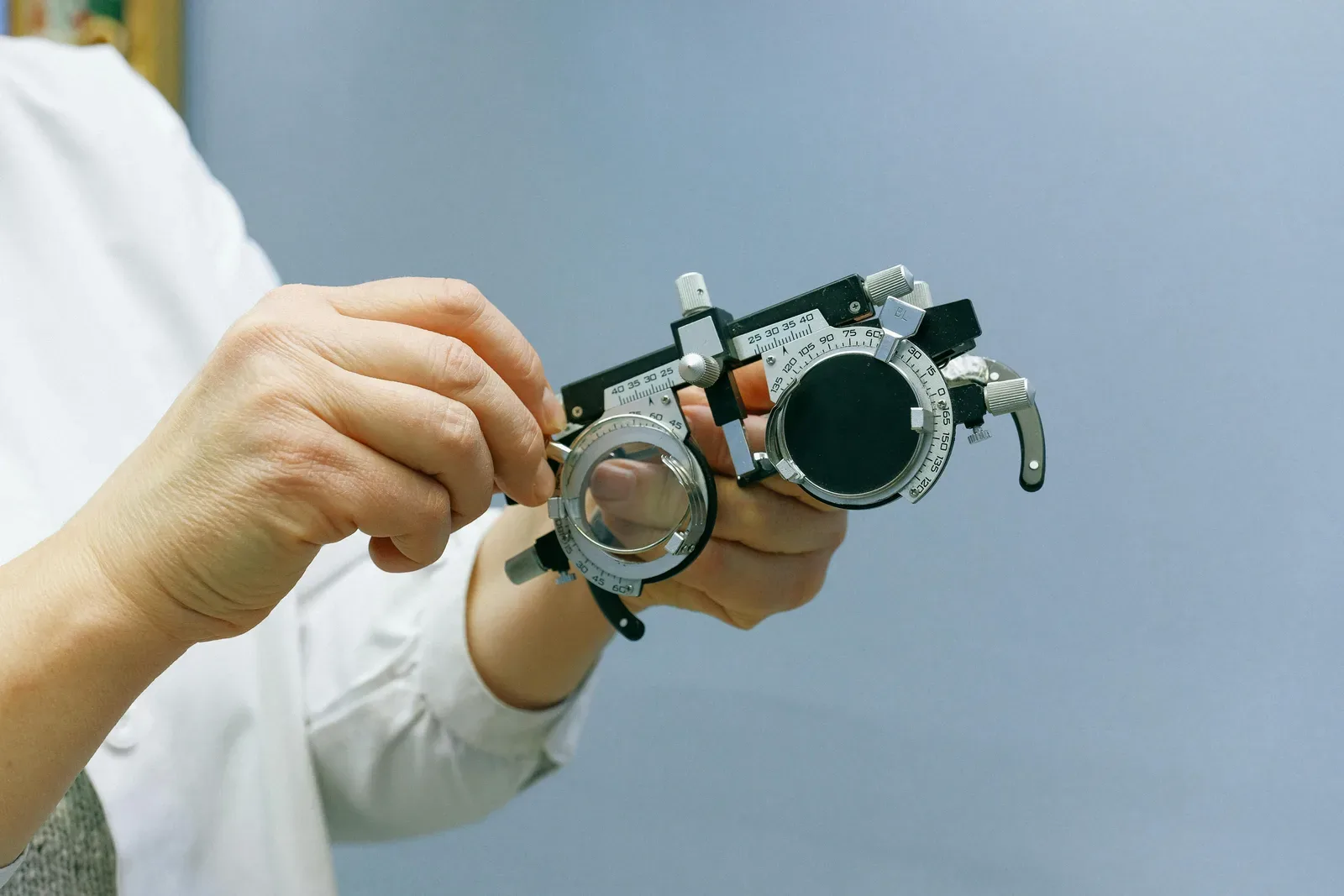 Crop unrecognizable doctor in white coat standing on blue background and showing vision test glasses with metal and plastic parts and measuring scale