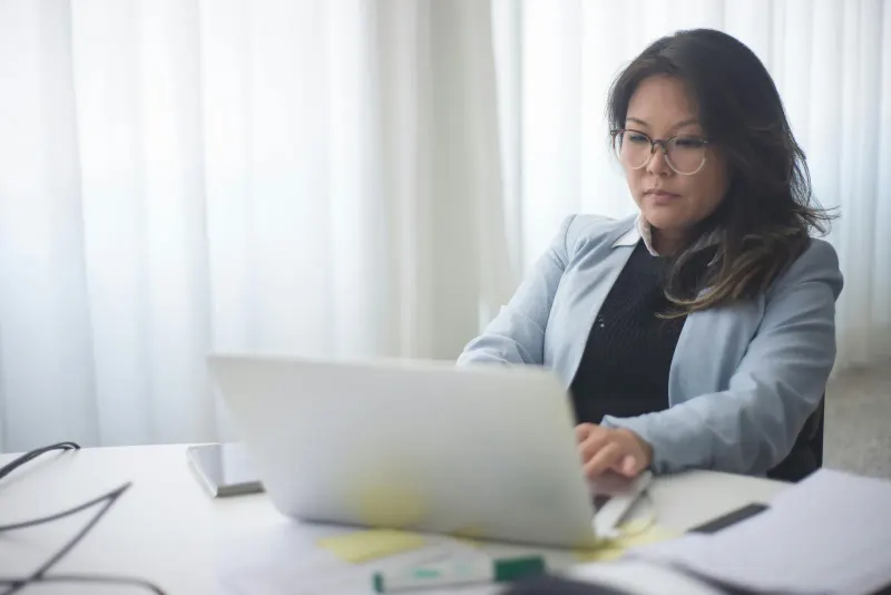 Focused businesswoman in office working on laptop with documents on the desk.