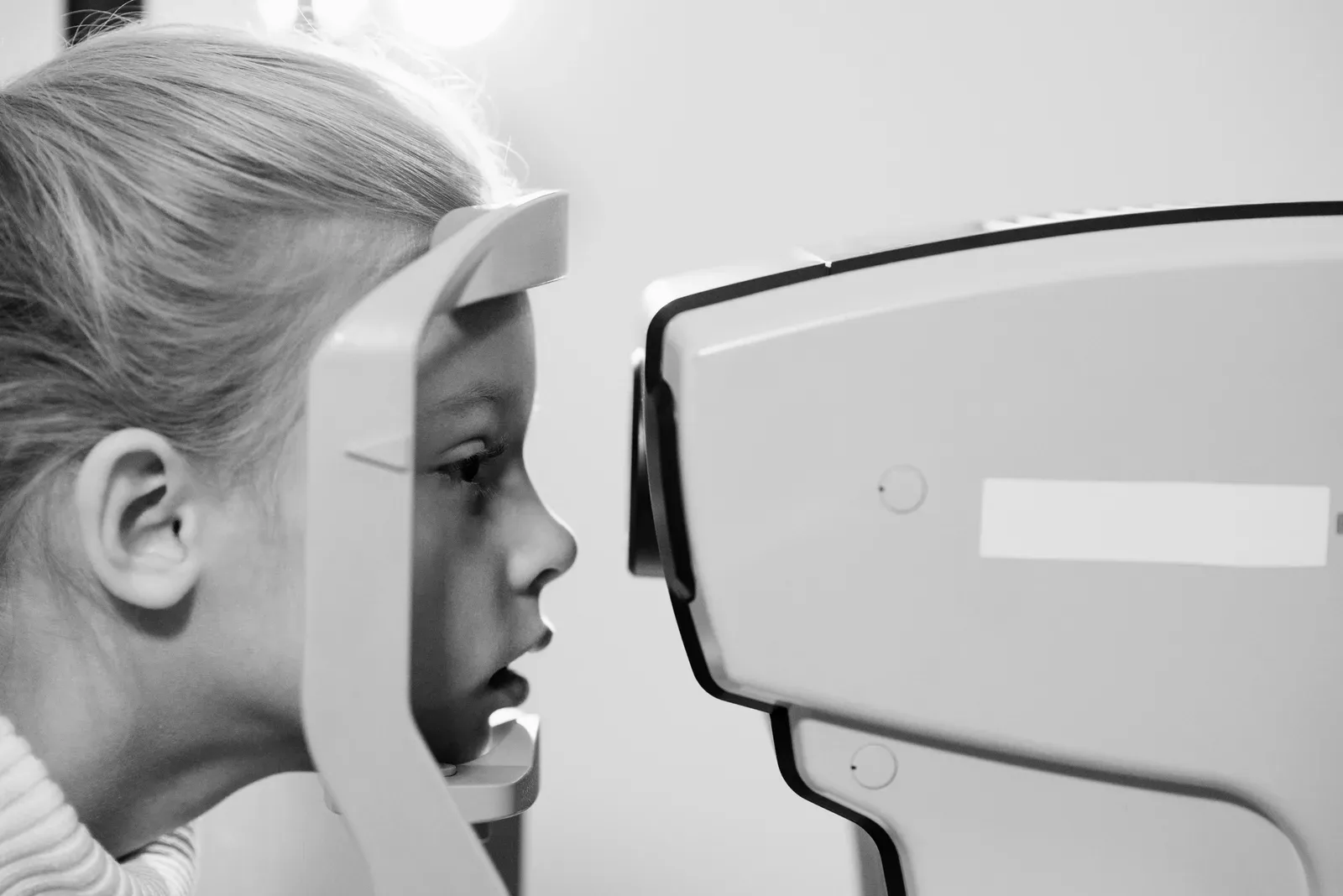 A young girl undergoes an eye examination using advanced medical equipment in a grayscale setting.