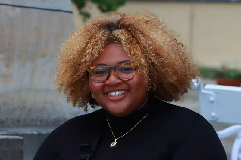 A joyful woman with curly hair and glasses smiling outdoors in Prague.