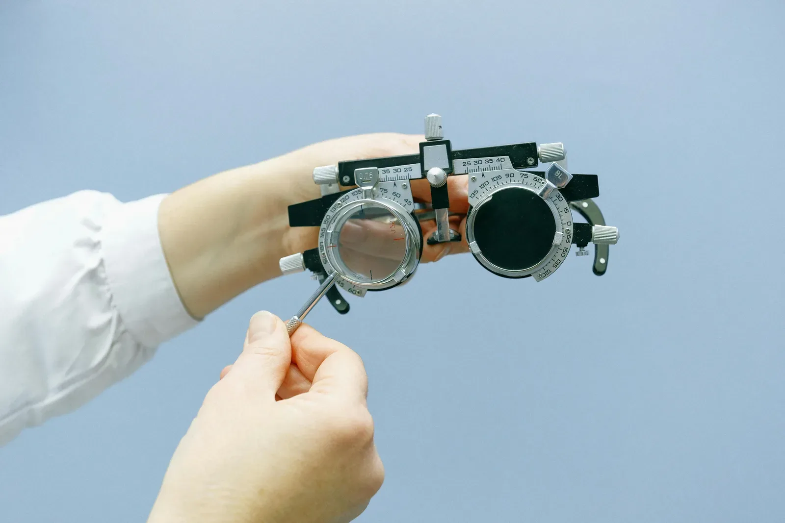 Crop anonymous ophthalmologist setting eye vision test glasses with magnifying glass and numeral scale in blue background