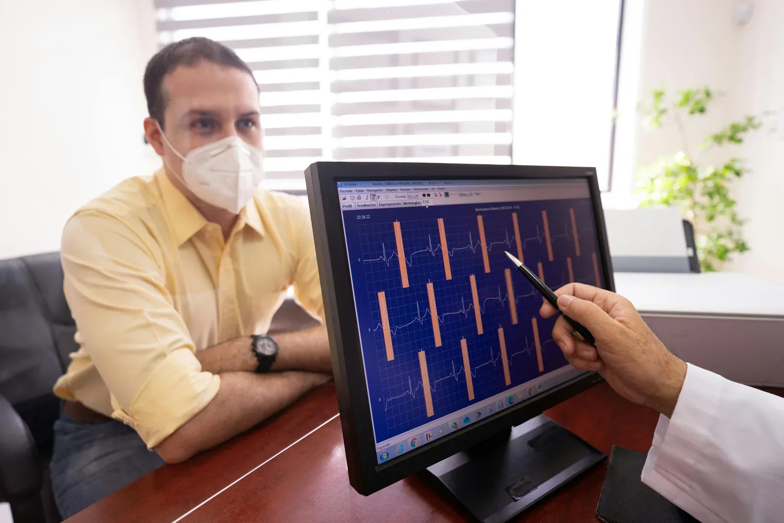 Medical consultation as a doctor reviews ECG results with a masked patient in a clinic setting.