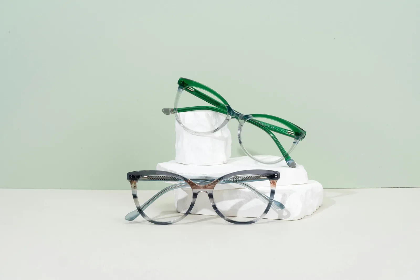 Minimalist eyeglasses display with green and transparent frames on a pastel background.