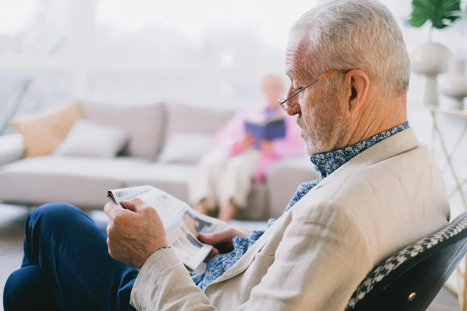 Elderly man in glasses reading newspaper at home with serene atmosphere.