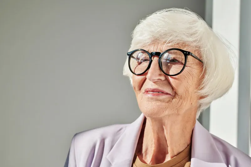 Portrait of a senior woman smiling warmly with eyeglasses and white hair indoors.