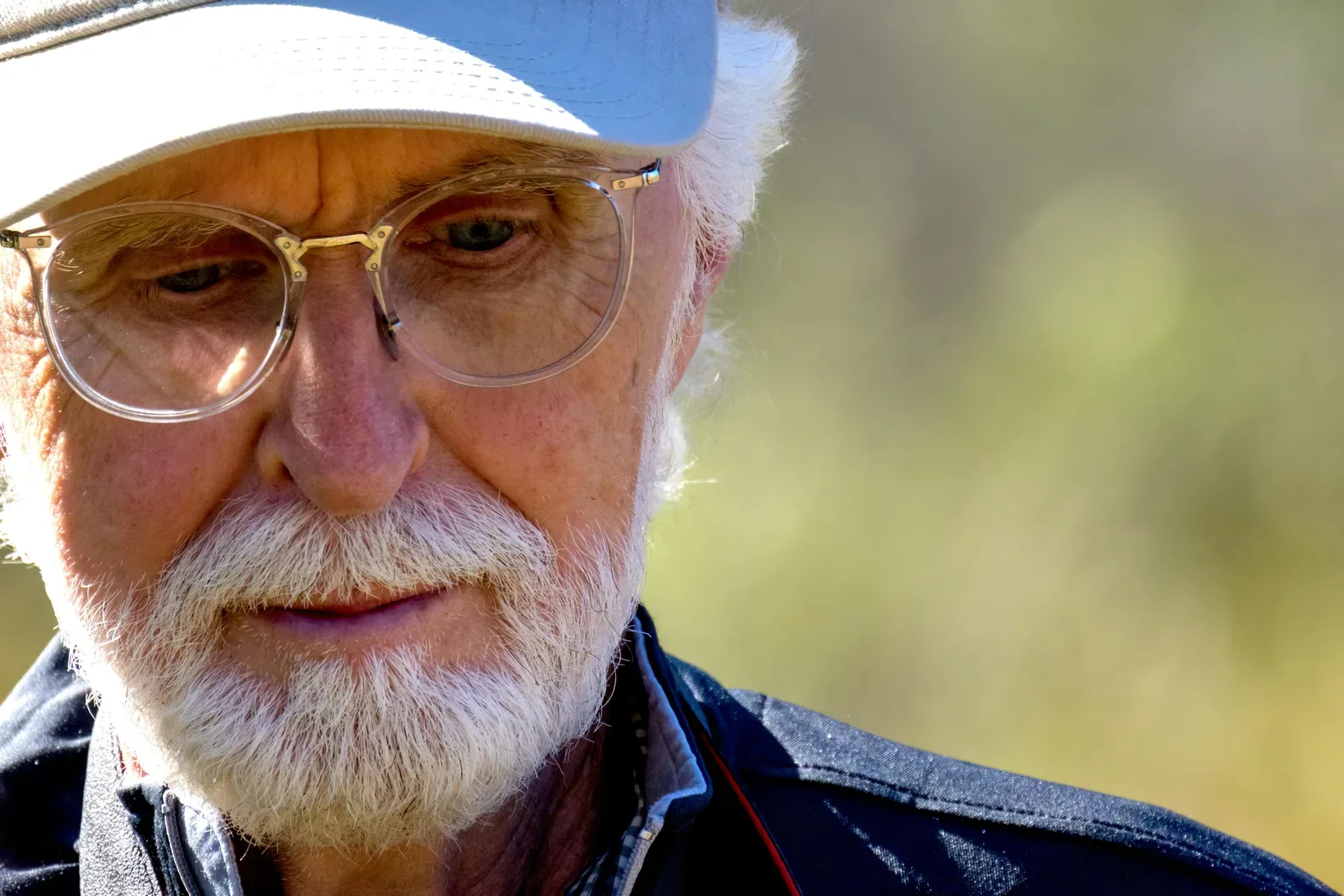 Close-up portrait of an elderly man in a cap and eyeglasses enjoying a sunny day outdoors.