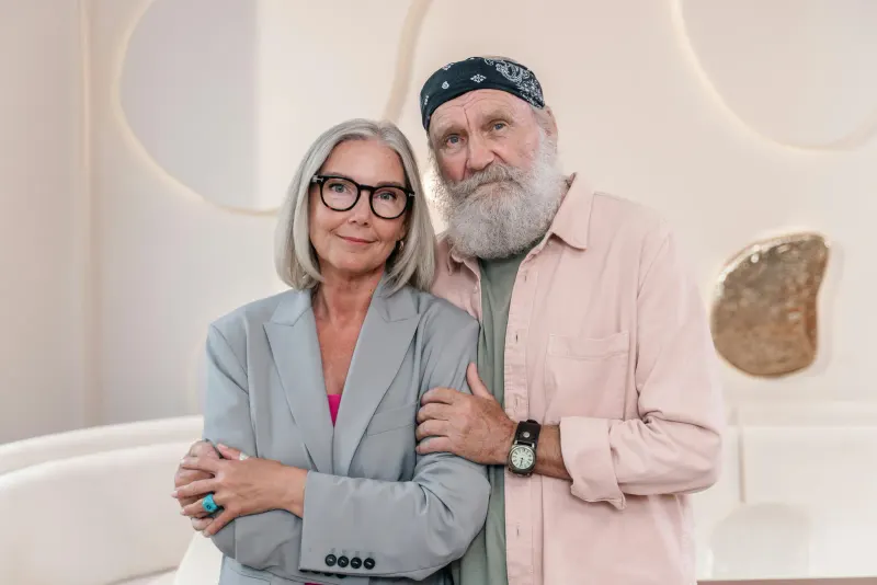 Elderly couple embracing indoors, showcasing fashion and warmth.