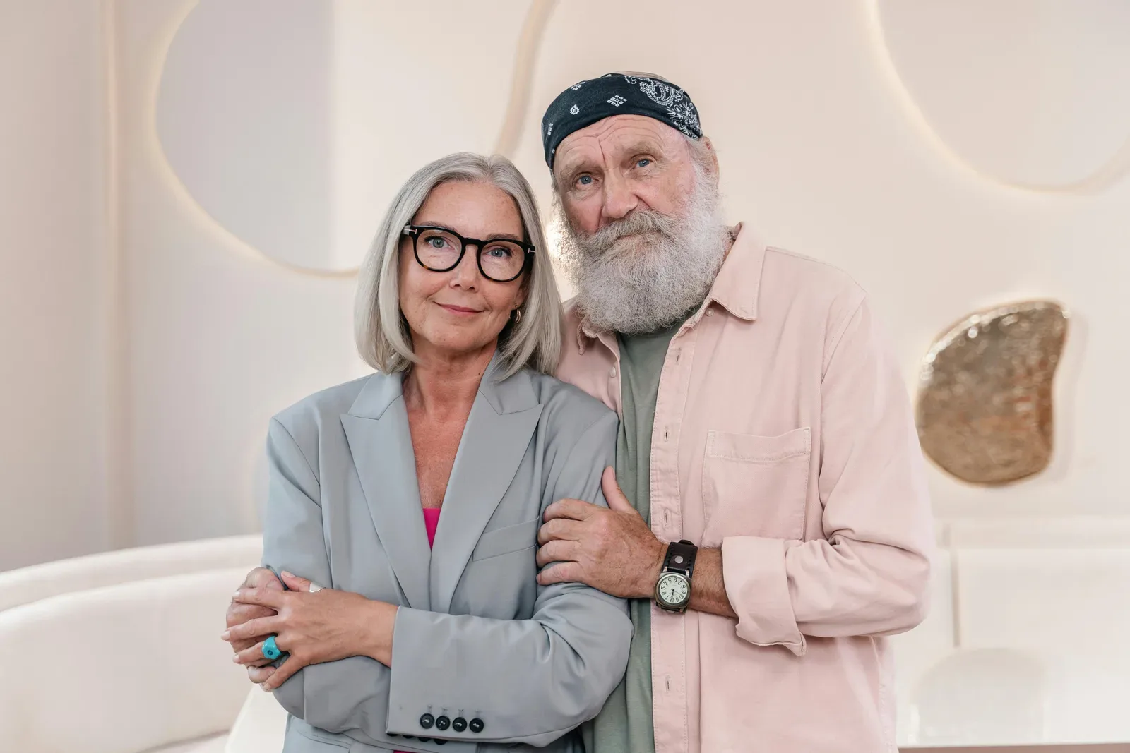 Elderly couple embracing indoors, showcasing fashion and warmth.