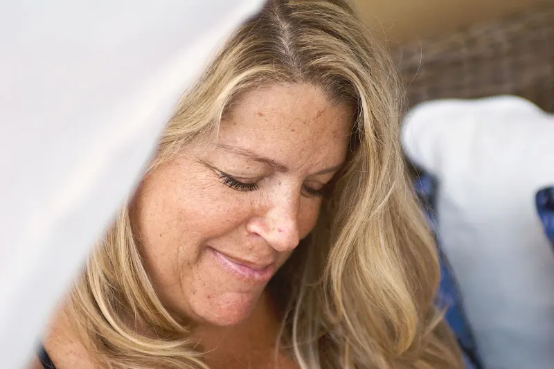 Close-up portrait of a serene woman with long blonde hair smiling gently and relaxing indoors.