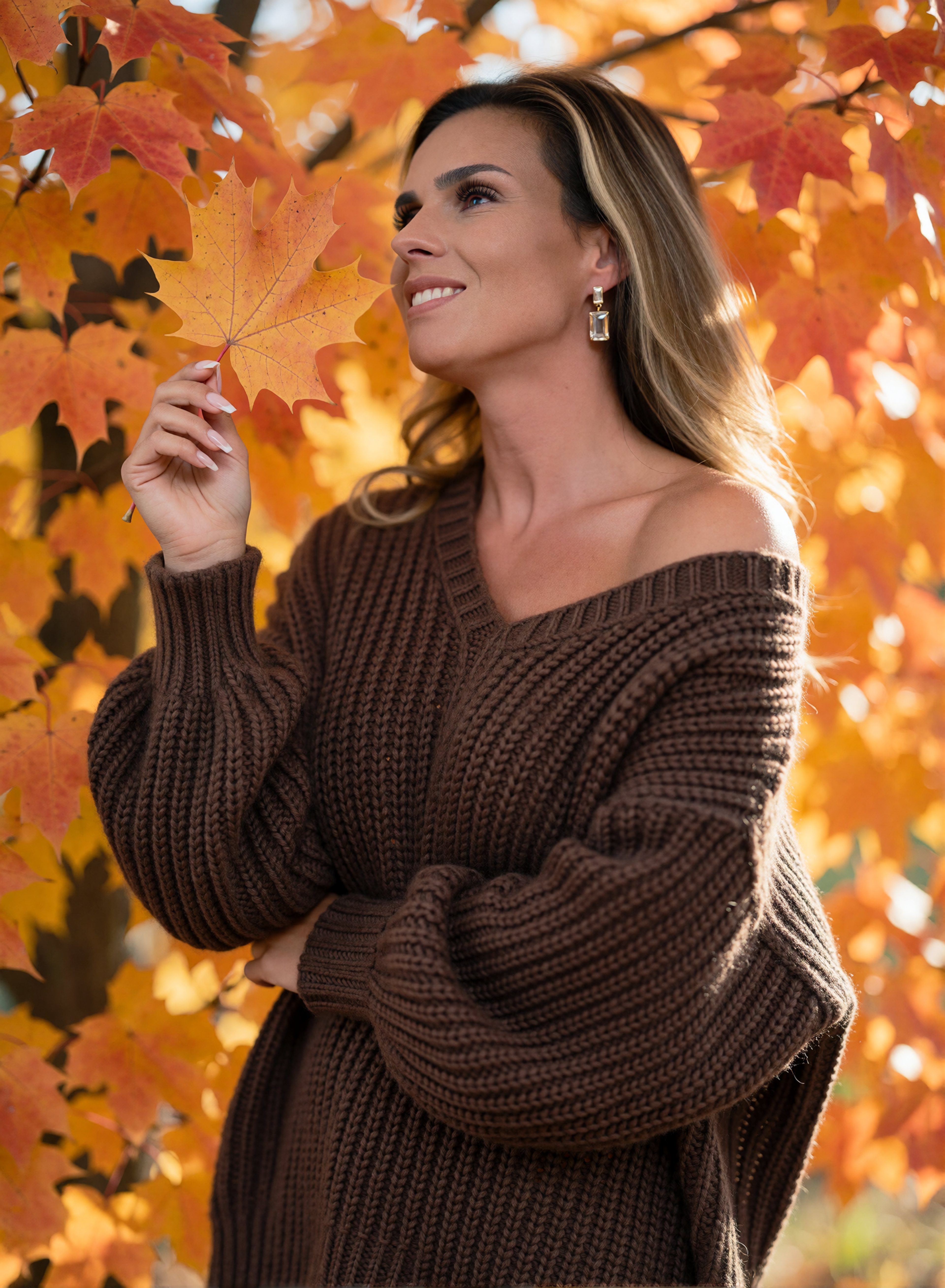 Digital twin Nicole Funken in a brown knitted sweater with a maple leaf in front of glowing autumn foliage.