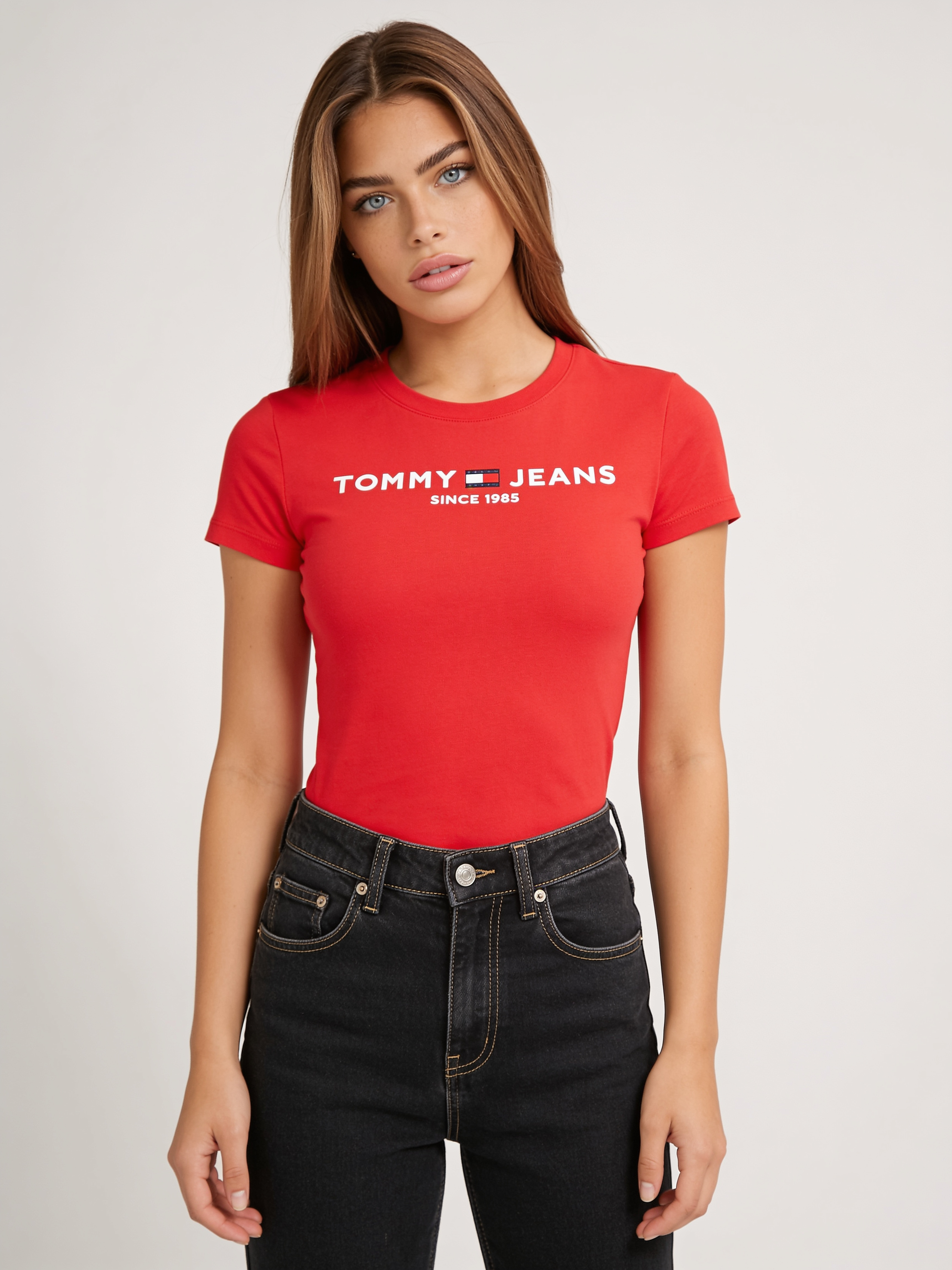 KI-Model im roten T-Shirt mit Logo-Print und schwarzer Jeans