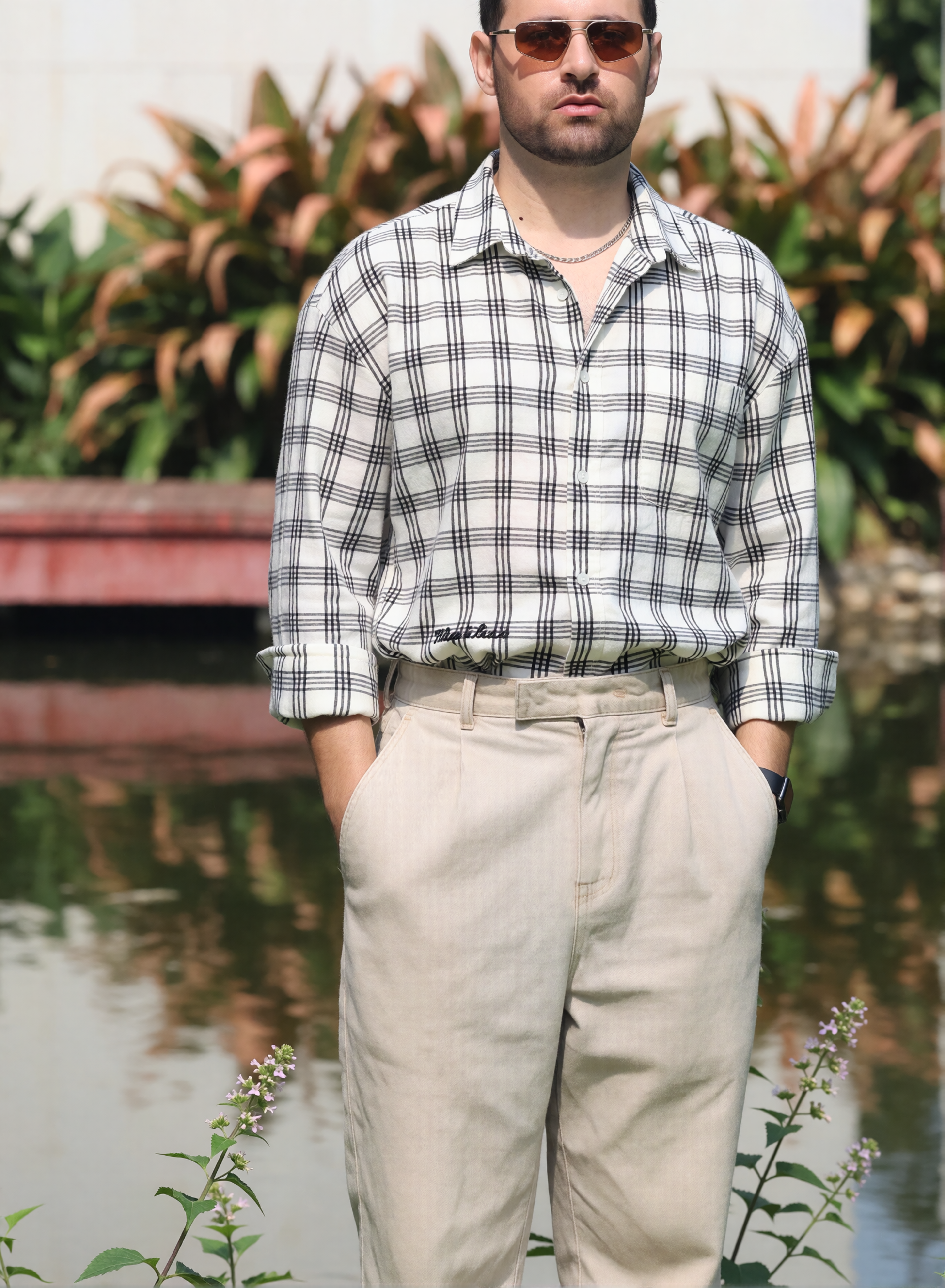 Digitaler Zwilling von Bruno Dias mit Sonnenbrille, kariertem Hemd und heller Bundfaltenhose vor einem Teich.