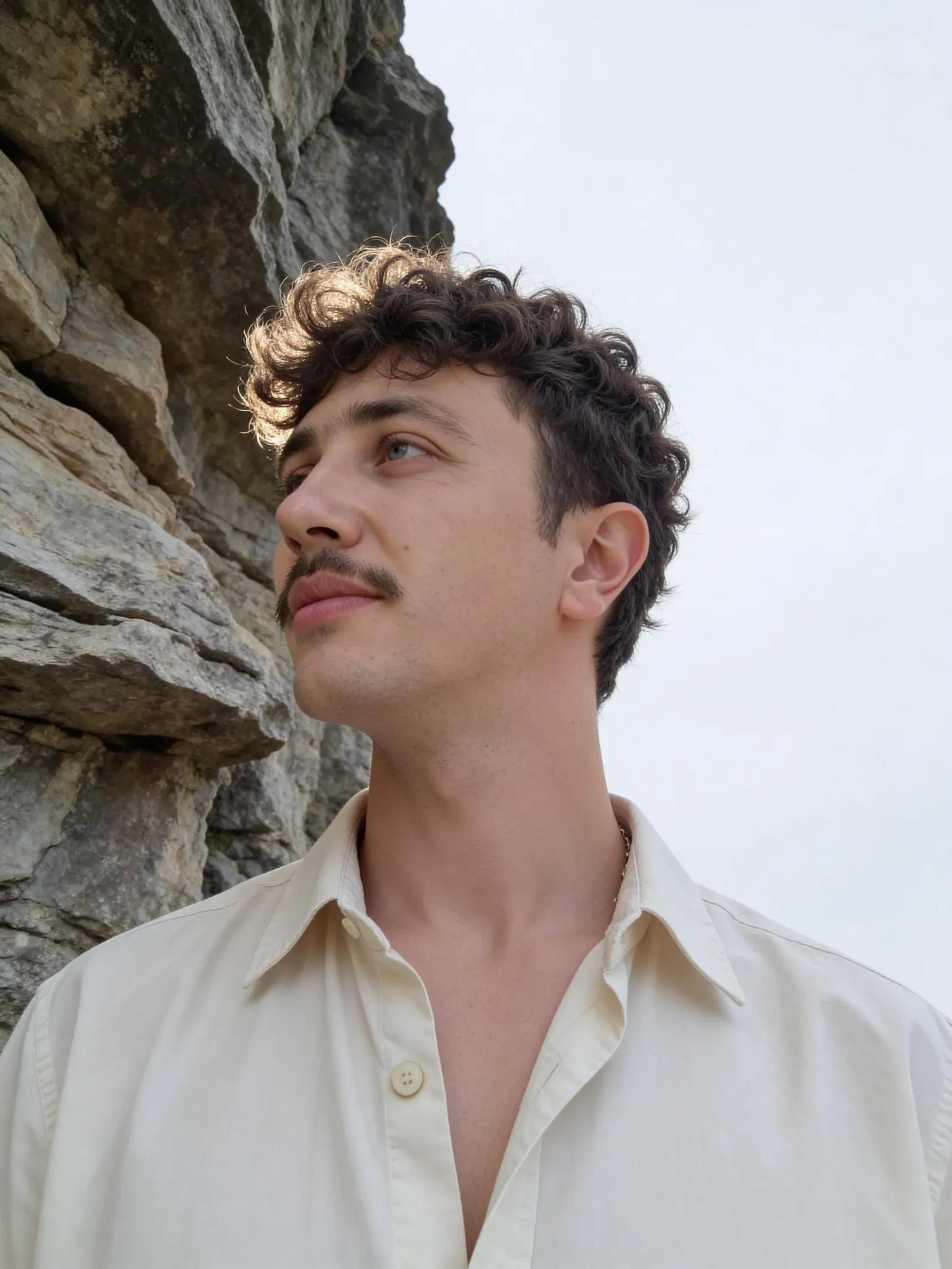 Artur Fenina im hellen Hemd vor einer Felswand, Blick nach oben