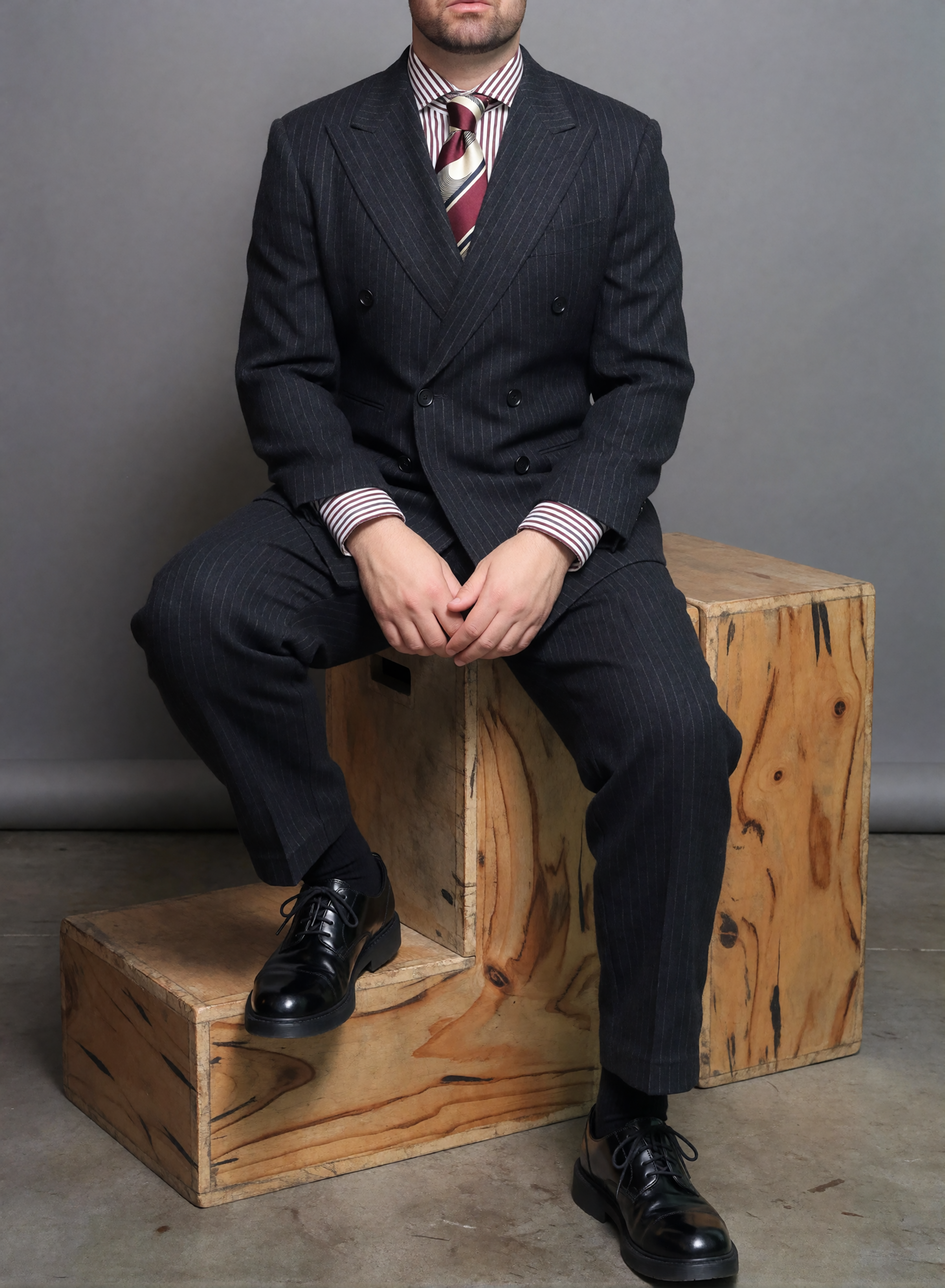 Digitaler Zwilling von Bruno Dias im dunklen Nadelstreifenanzug mit gestreiftem Hemd und Krawatte, sitzend auf Holzkisten im Fotostudio.