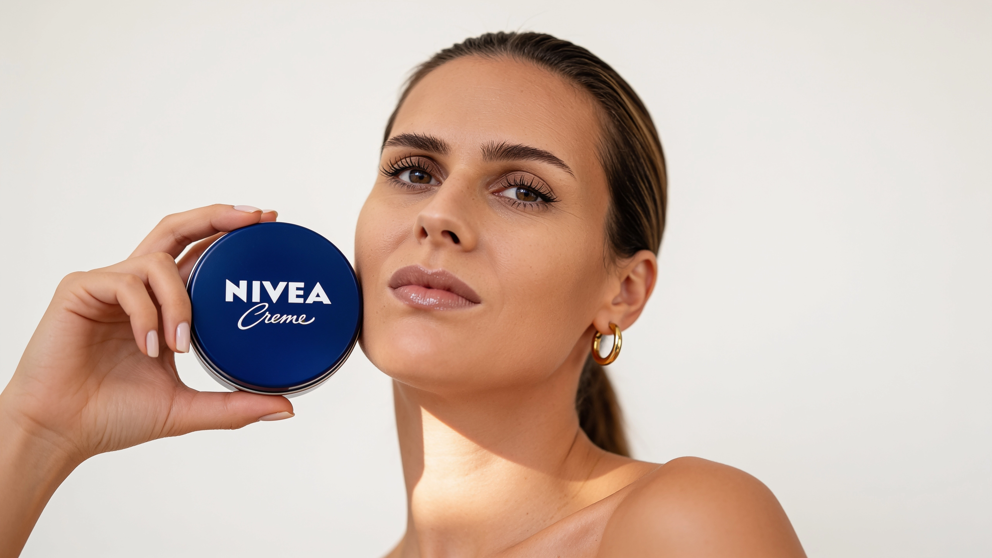 KI-Model hält eine blaue Cremedose an die Wange, Blick zur Seite