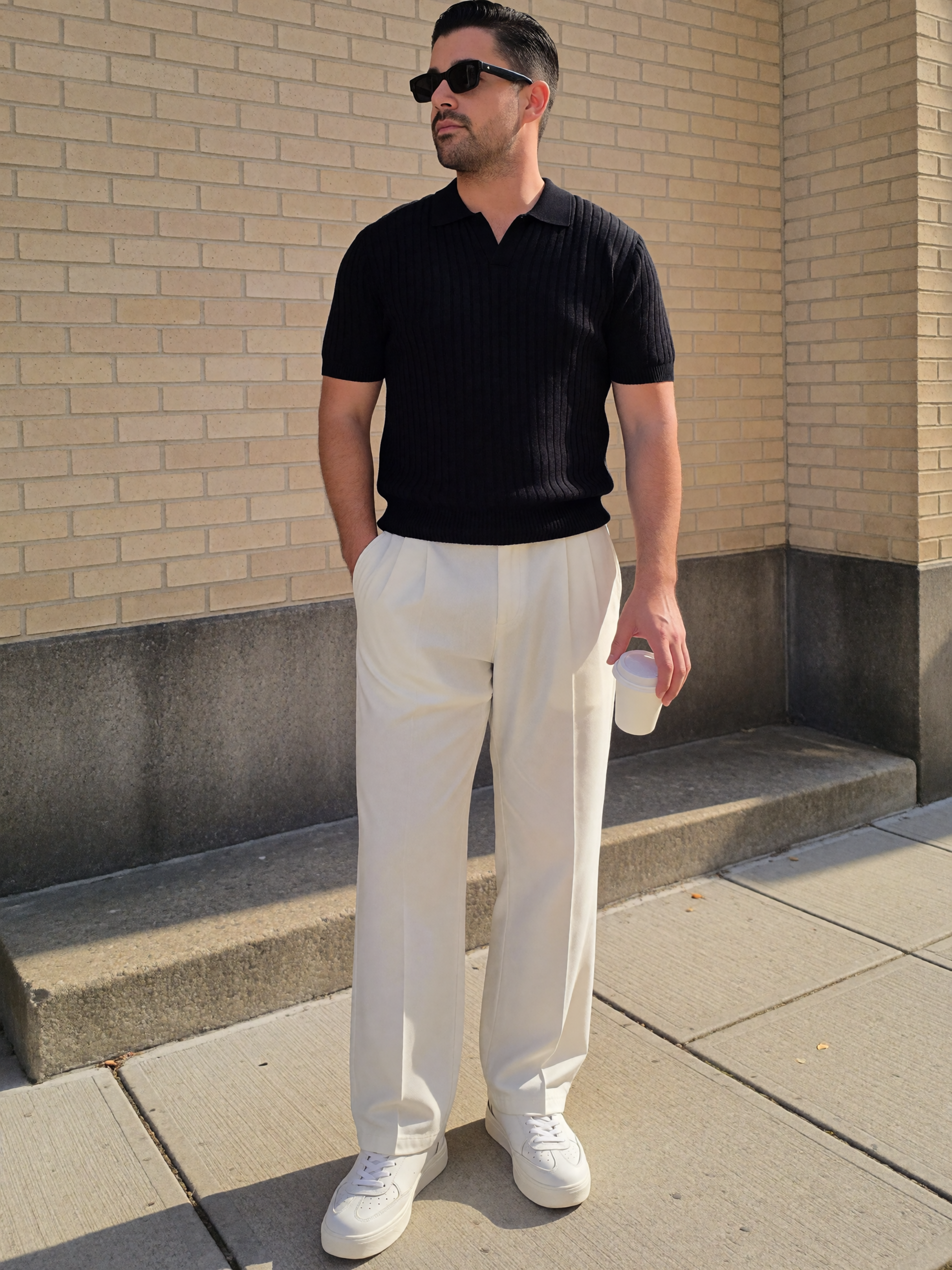 Digitaler Zwilling von Mousaab Ainouche in schwarzem Strick-Poloshirt, weißer Stoffhose, weißen Sneakern und Sonnenbrille bei einem modernen Outdoor-Fashion-Shooting.