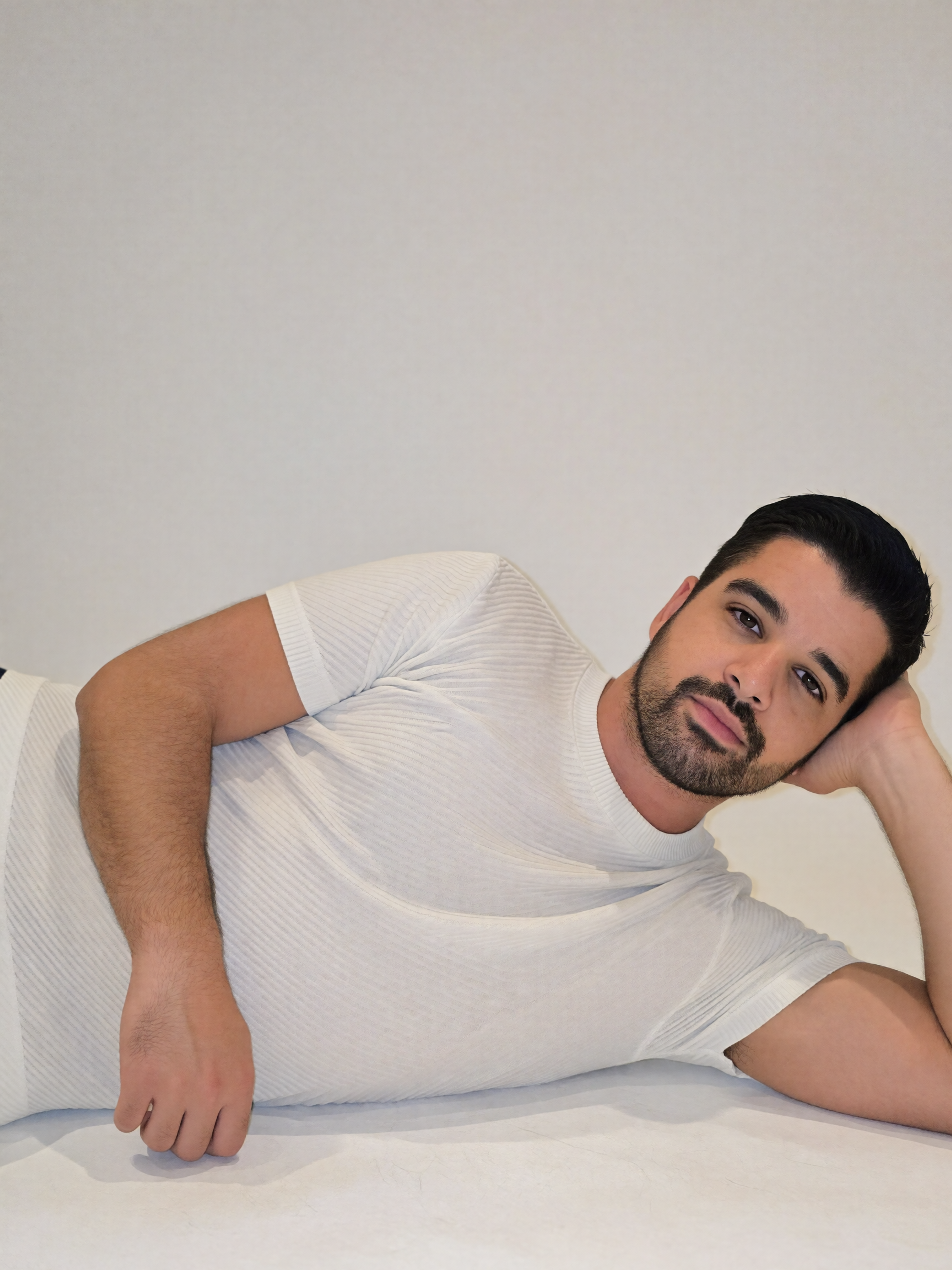 Digitaler Zwilling von Mousaab Ainouche in weißem geripptem T-Shirt, seitlich liegend vor hellem Hintergrund bei einem minimalistischen Fashion- und Portrait-Shooting.