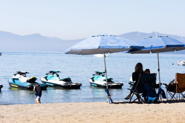 Rental jet skis lined up near the shore beside beach umbrellas