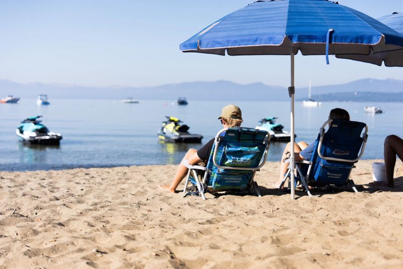 Beach chairs under an umbrella on the sand, with jet skis on the water