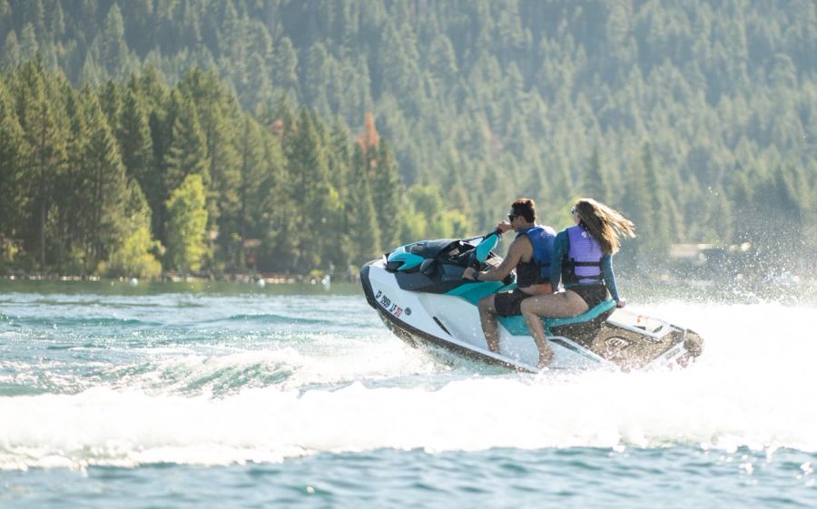 Two people riding a jet ski past the forested shoreline of Lake Tahoe