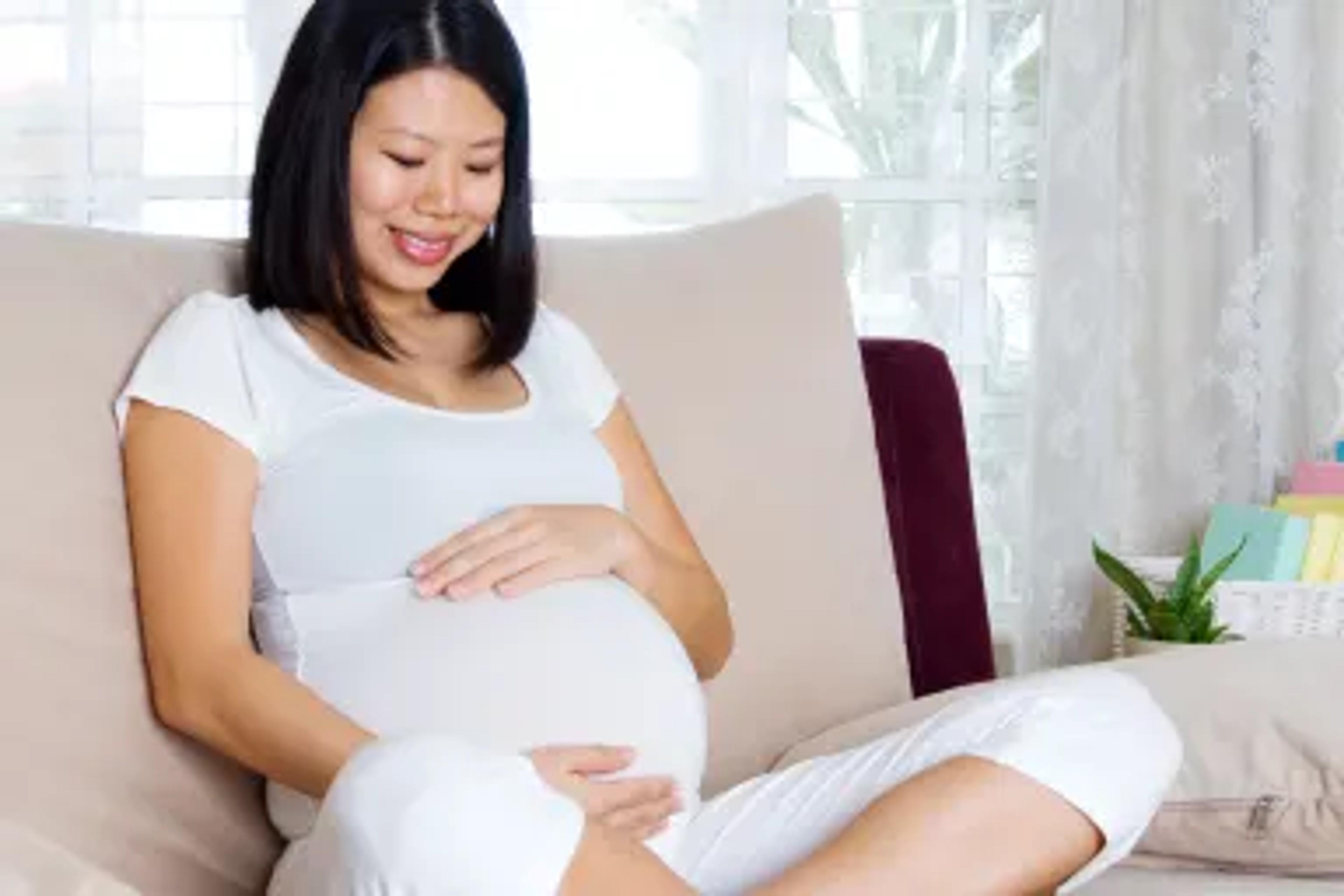 a pregnant woman is sitting on a couch holding her belly .