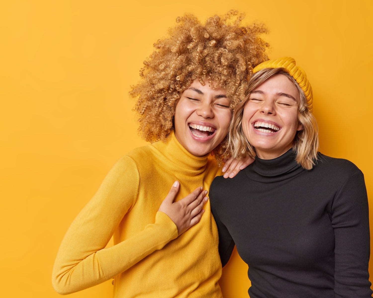 two women are laughing together in front of a yellow background .