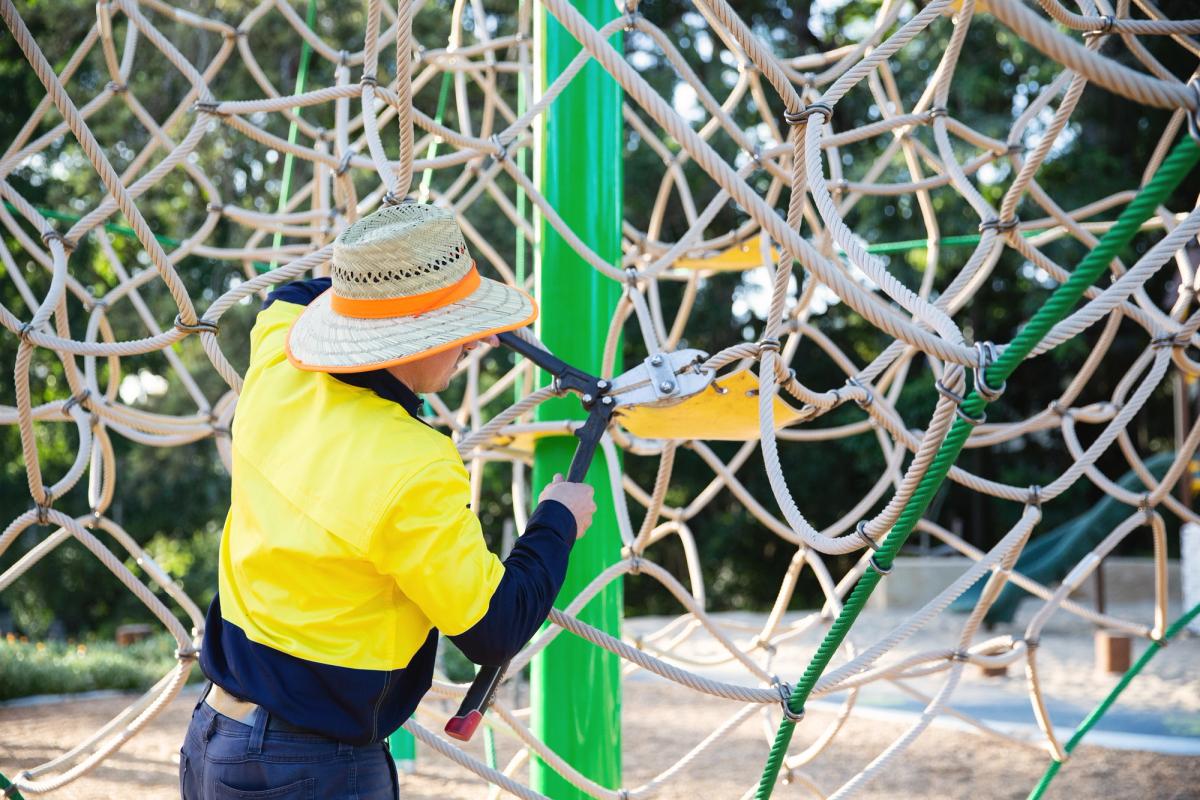 A Play Force employee performing maintenance on climbing play equipment made of rope.