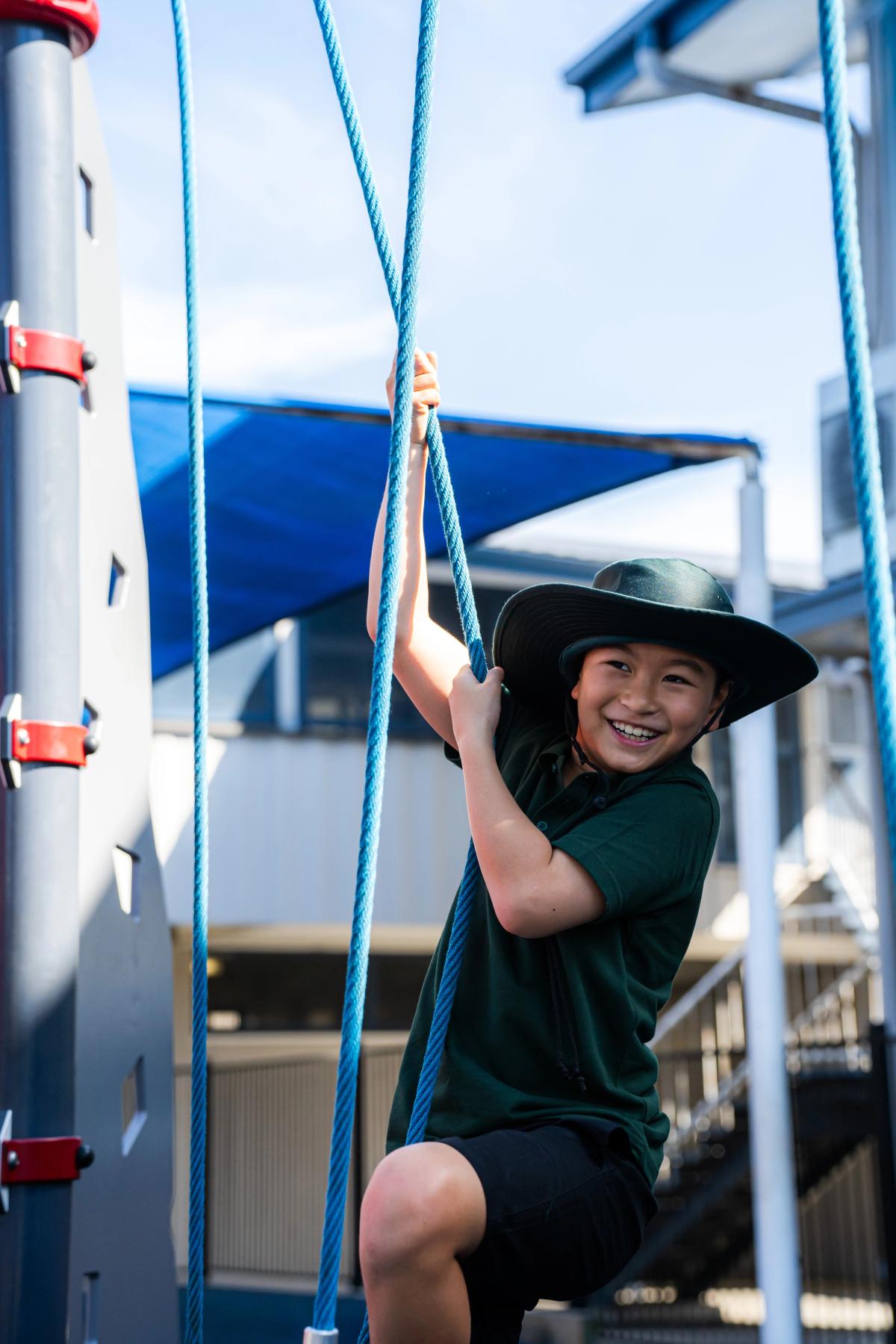 A child is smiling as they play on playground ropes, confidently exploring how to navigate through the play equipment.