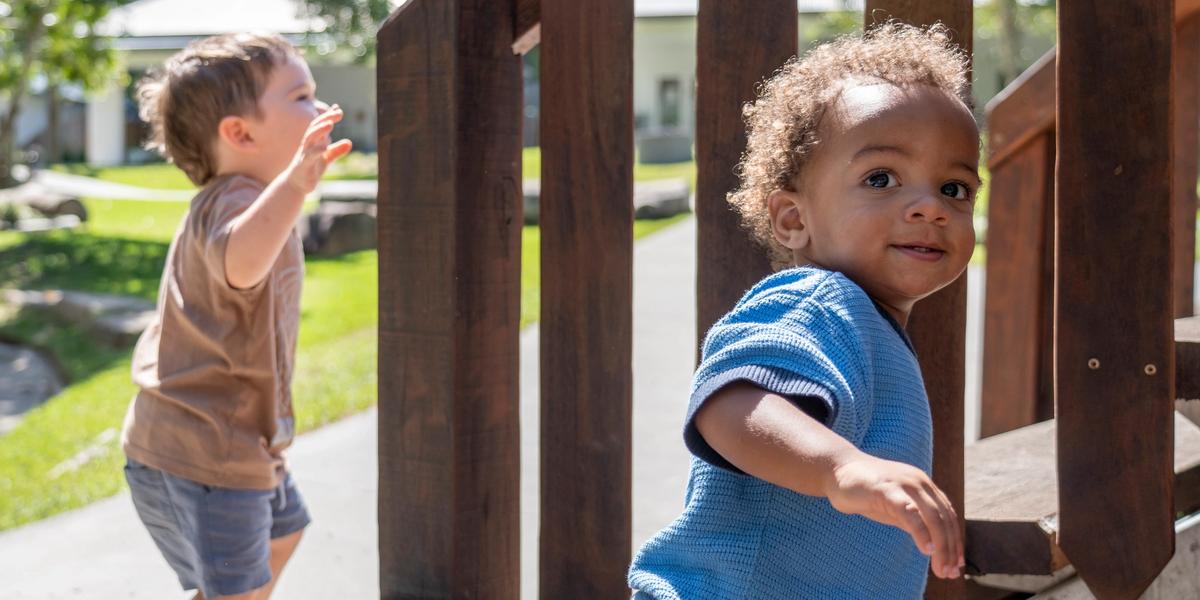 Two small toddlers playing on a playground at a daycare centre.