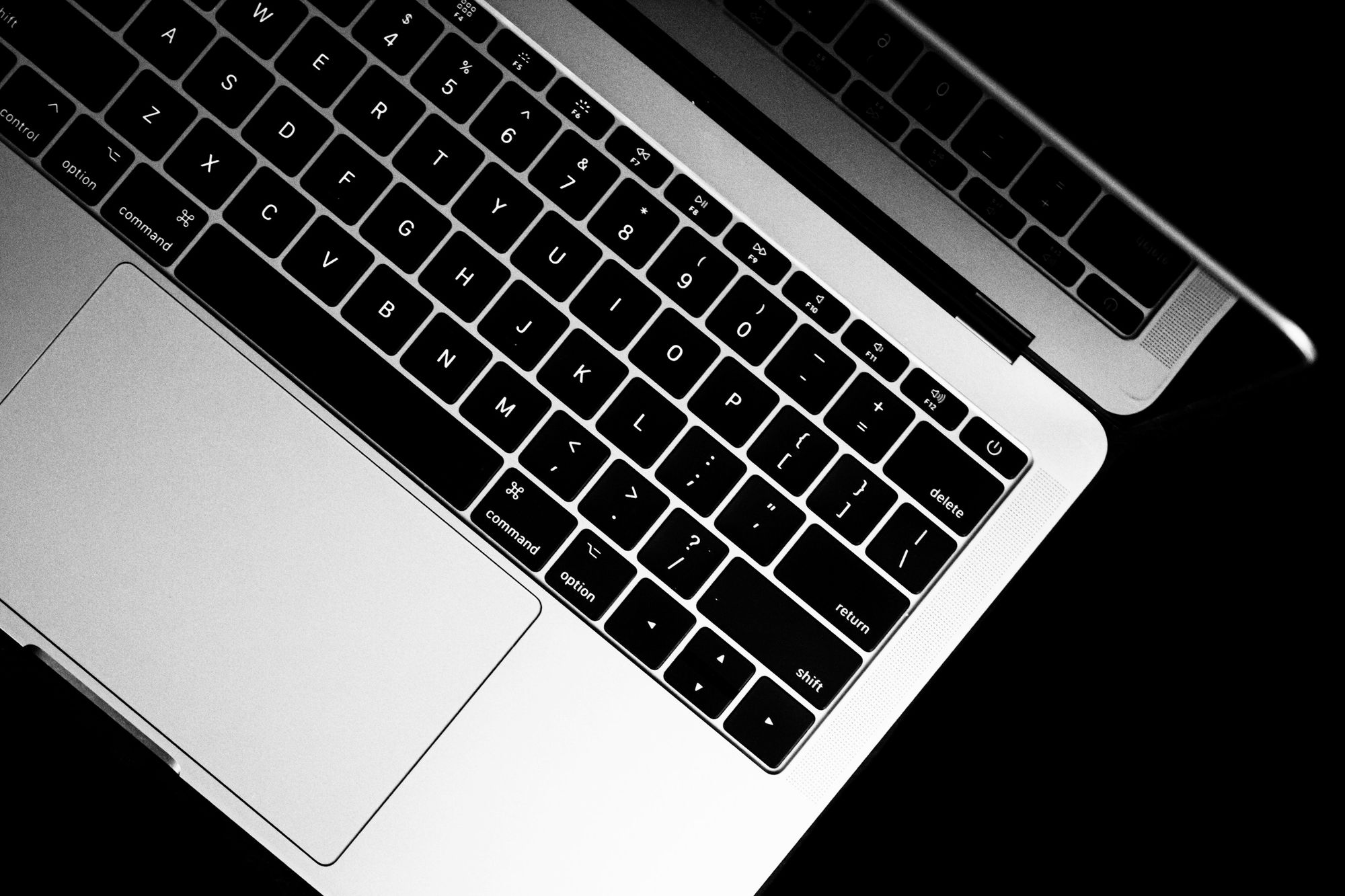 黒い背景に置かれたノートパソコンのキーボードを斜め上から写したモノクロ写真