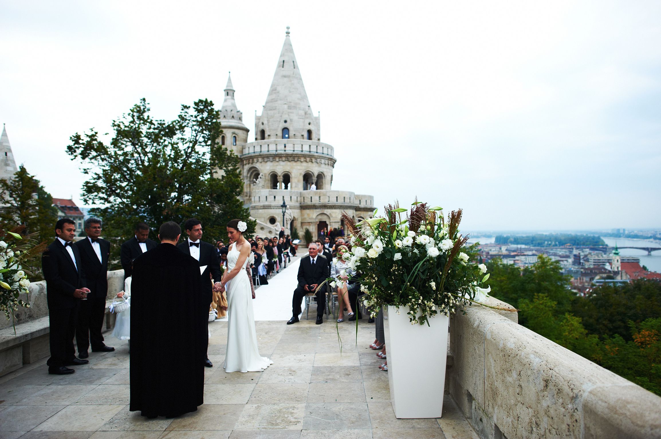 Brudepar under vielse ved Fisherman’s Bastion i Budapest, omgitt av historiske tårn og utsikt over byen.