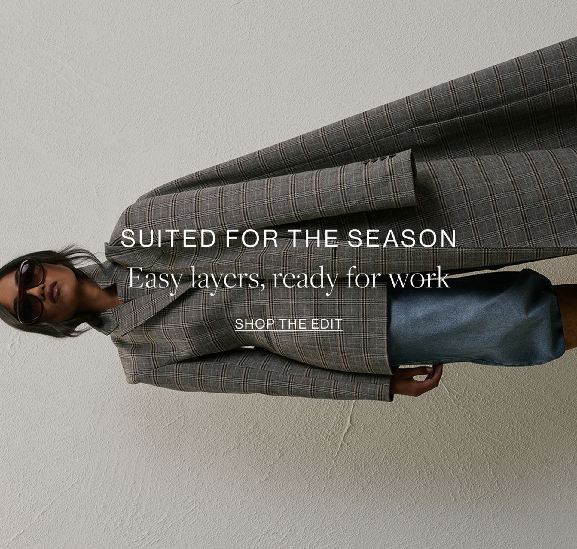 Model wearing a grey plaid print blazer and blazer coat. Text overlay: "SUITED FOR THE SEASON. Easy layers, ready fork work"