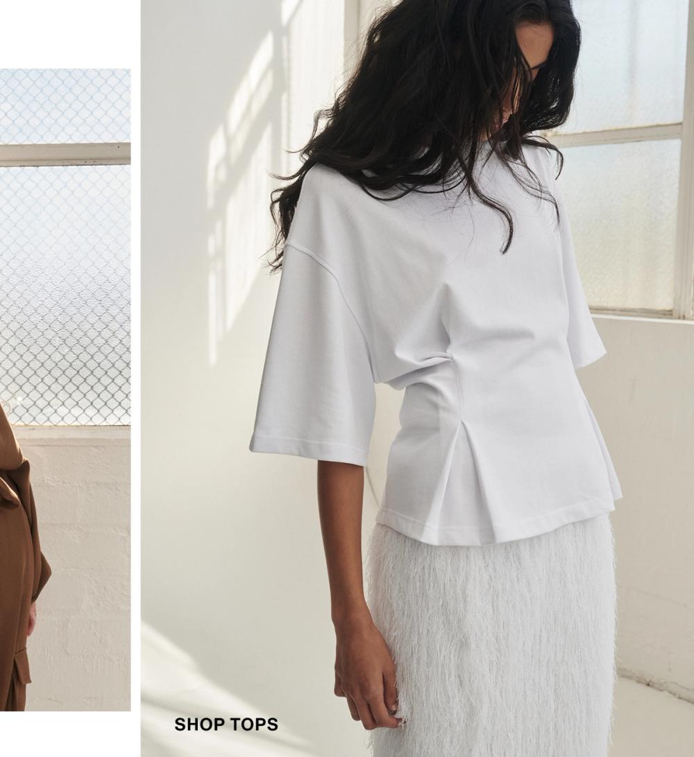 Model posing wearing a white tee. SHOP TOPS.