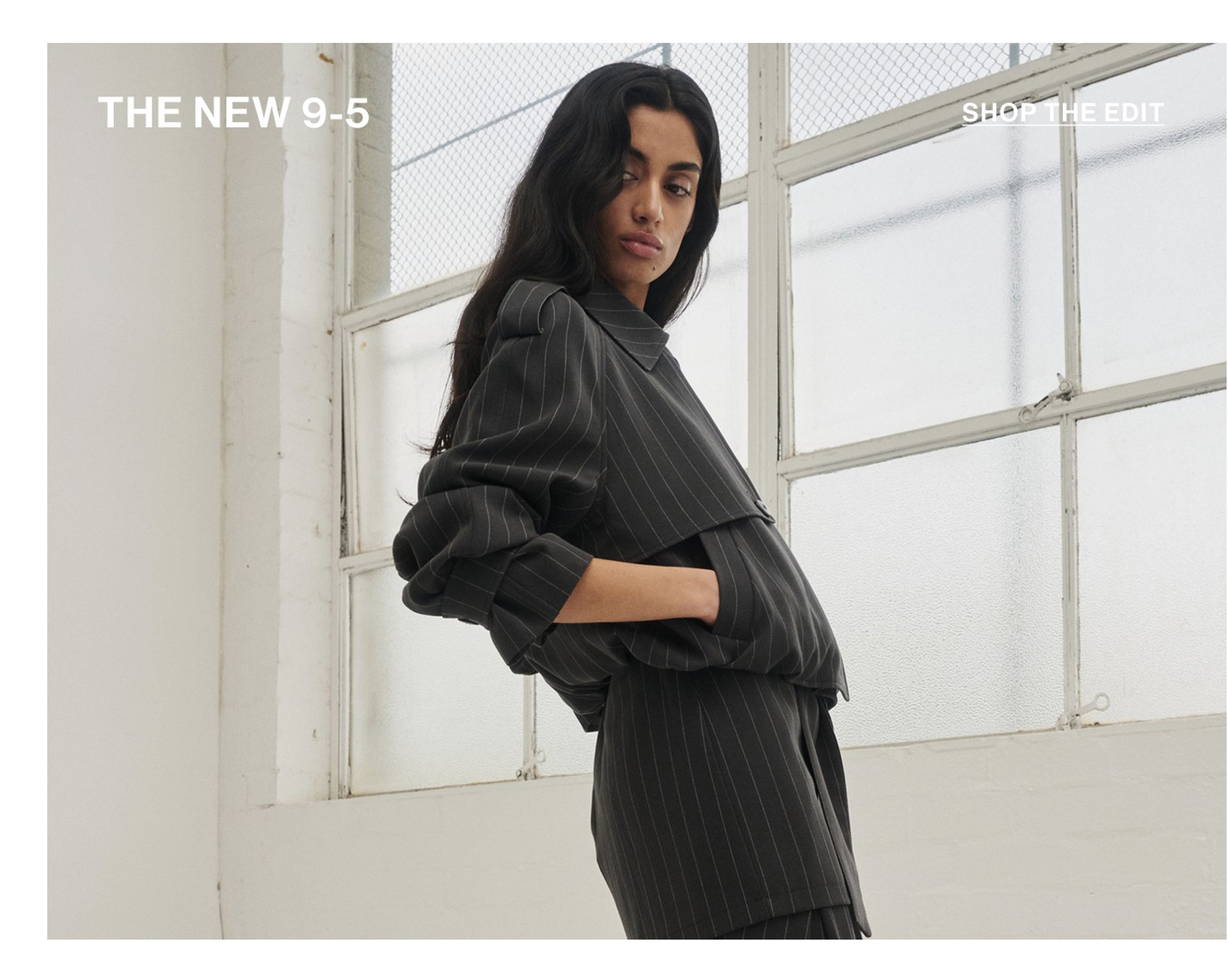 Model standing with hand in her pockets wearing an almond cropped trench jacket with text overlay: "THE NEW 9-5""