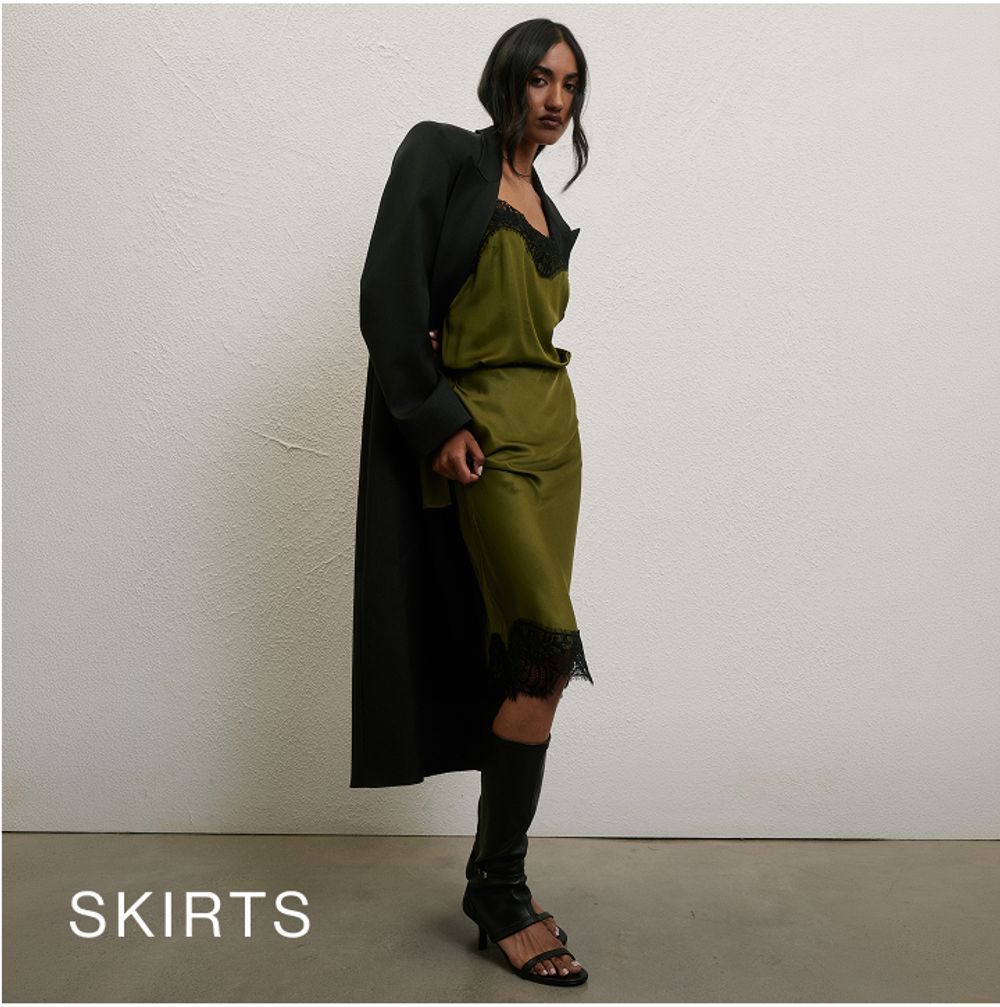 Model wearing a satin green skirt with black lace detailing. SHOP SKIRTS.