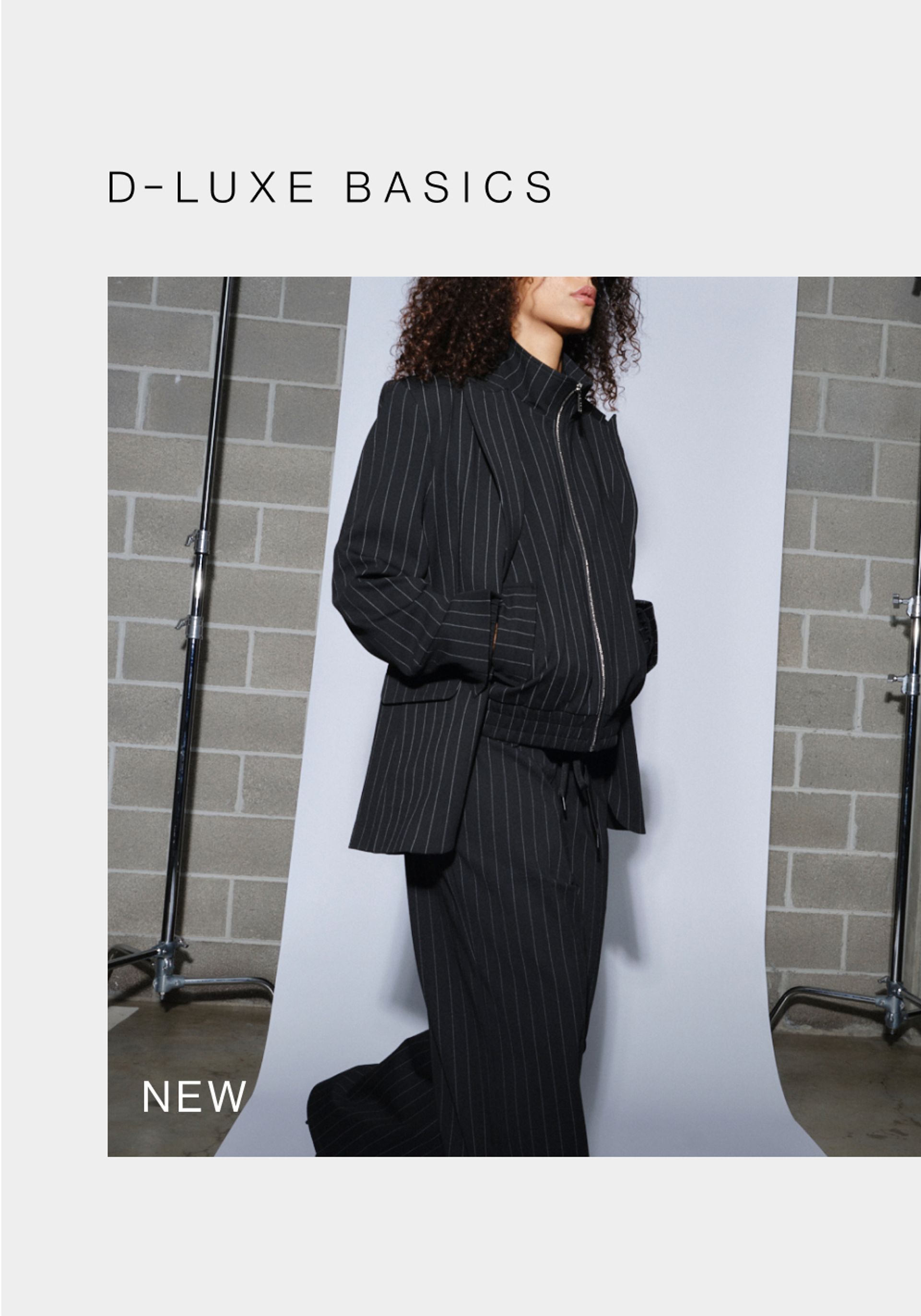Model wearing black pinstripe suit in a studio. SHOP NEW D-LUXE.