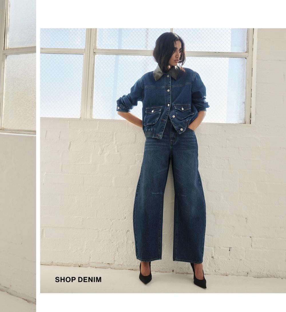 Model posing in a blue denim set in a studio. SHOP DENIM.