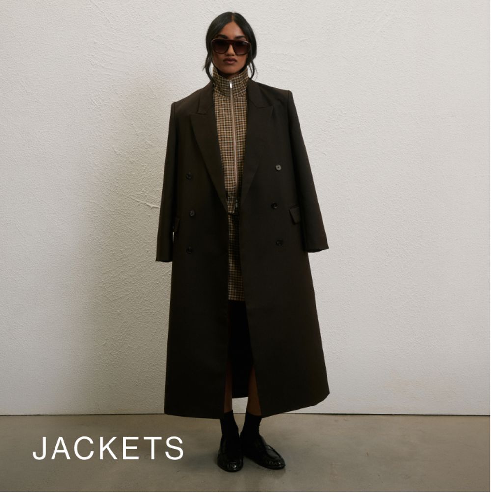 Model wearing a brown blazer coat against a neutral background. SHOP JACKETS.